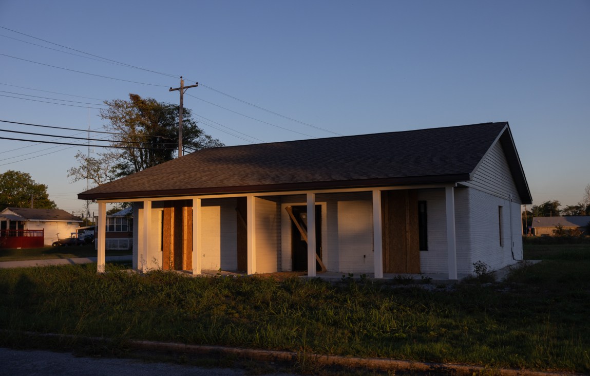 Sunset light illuminates an unfinished house that is partially boarded up.