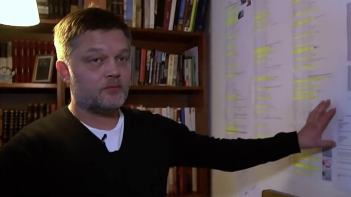 Photo of Johannes Kr Kristjansson, pointing at documents stuck up on a wall at his home in Iceland.