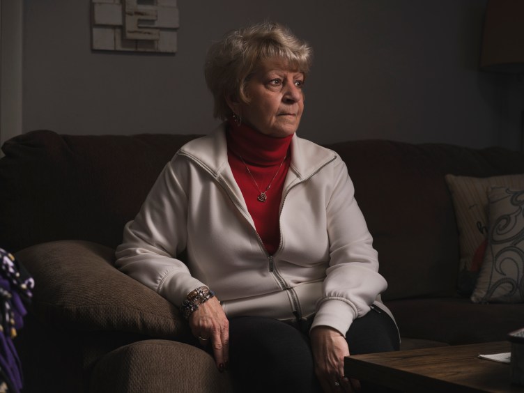 A woman on a living room sofa looks off to the side with a serious expression.
