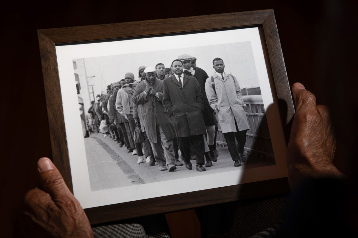 Hands hold a framed black-and-white photograph of a line of people walking across a bridge.