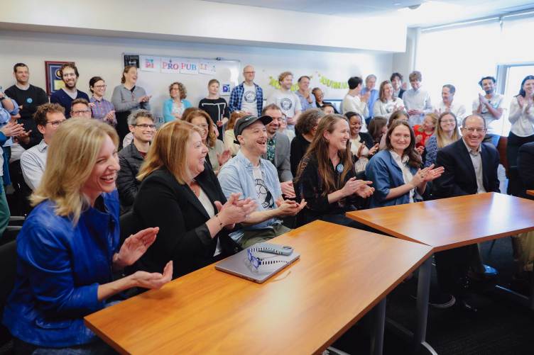 A large group of people smiling and clapping in an office conference room.