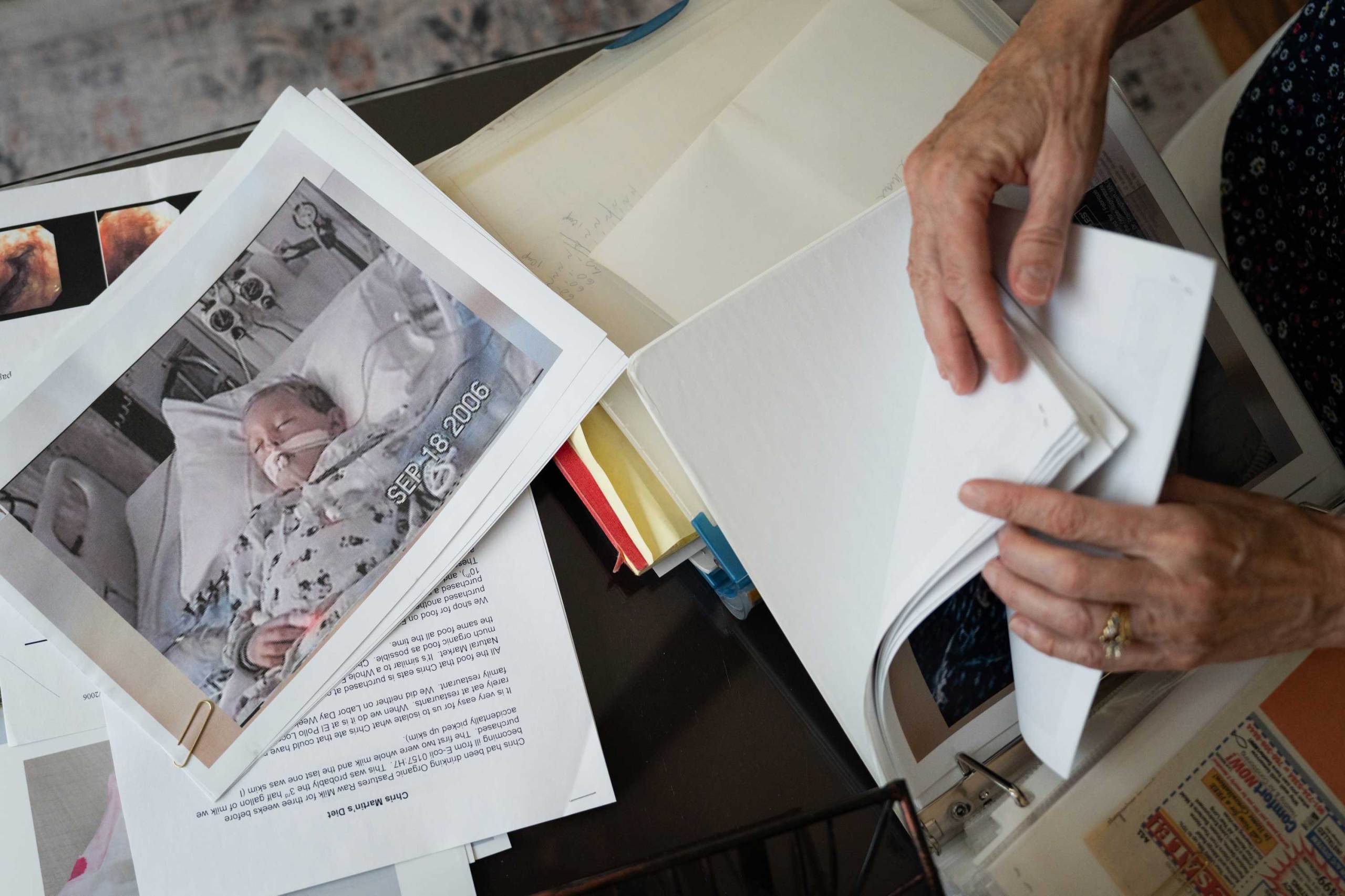 An overhead view of an older person’s hands flipping through a stack of documents and photos. Prominently displayed on the left is a printed photograph of a young child in a hospital bed with medical tubes attached.