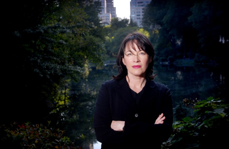 A woman stands in a park with her arms crossed, posing for the camera.