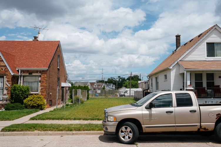 A row of houses and a parked truck, seen from the street. The center house is missing, and a patch of green lawn is in its place.