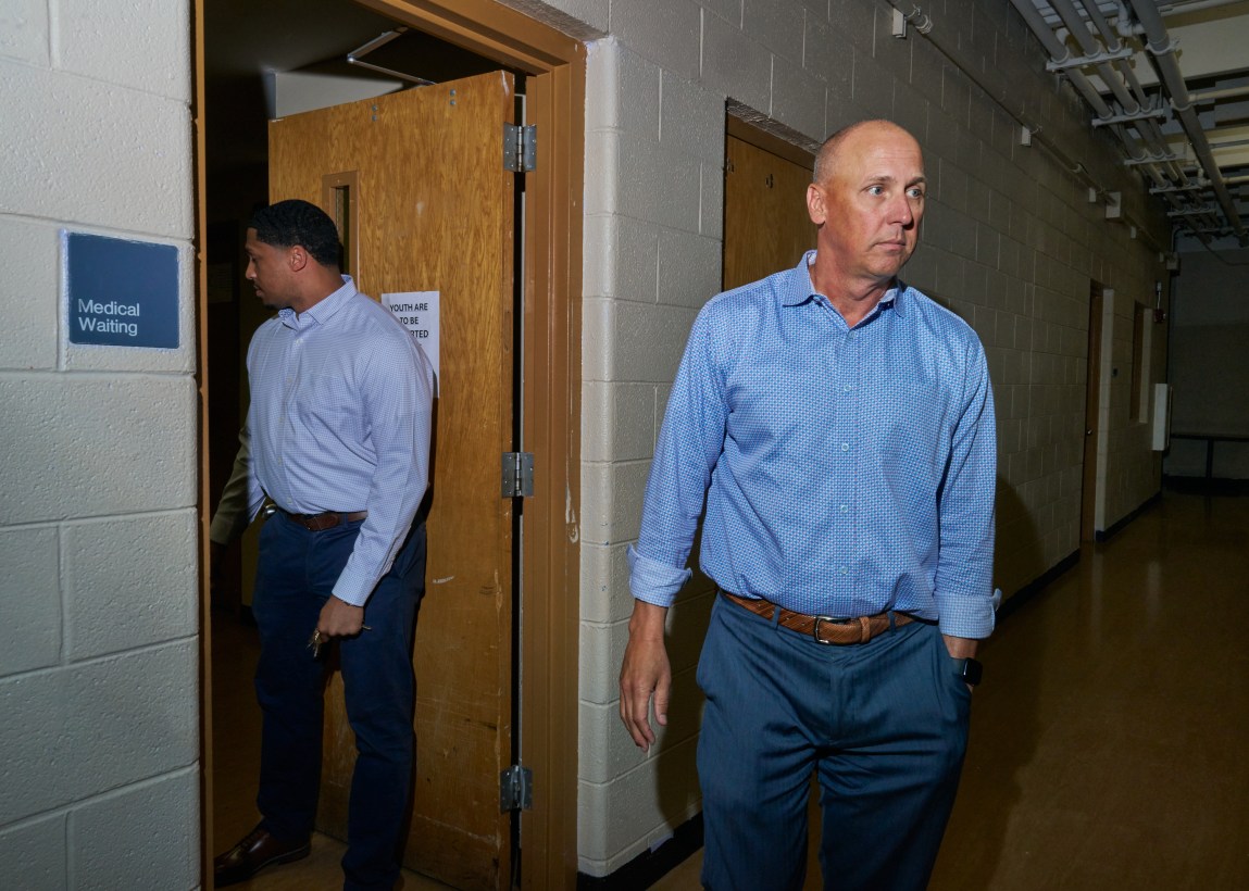 Two men in business attire in a hallway. A sign on the wall reads “Medical Waiting.”