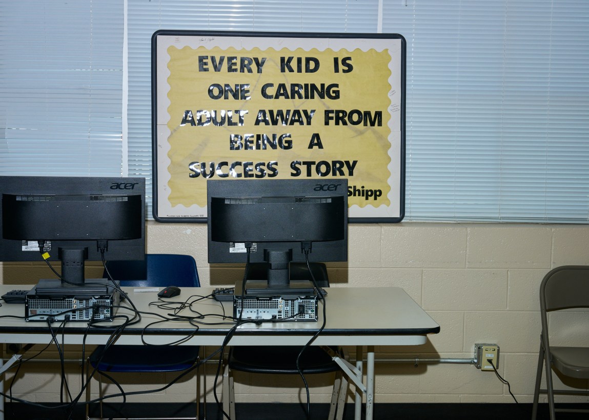 A room has two computers on a table and a sign that reads, “Every kid is one caring adult away from being a success story.”