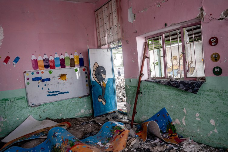 A colorful classroom with decorations for young children is in ruins after a bomb attack, with debris covering the floor.