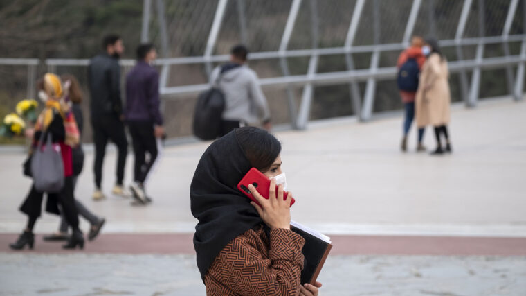 A woman stands on a bridge speaking on a red cell phone