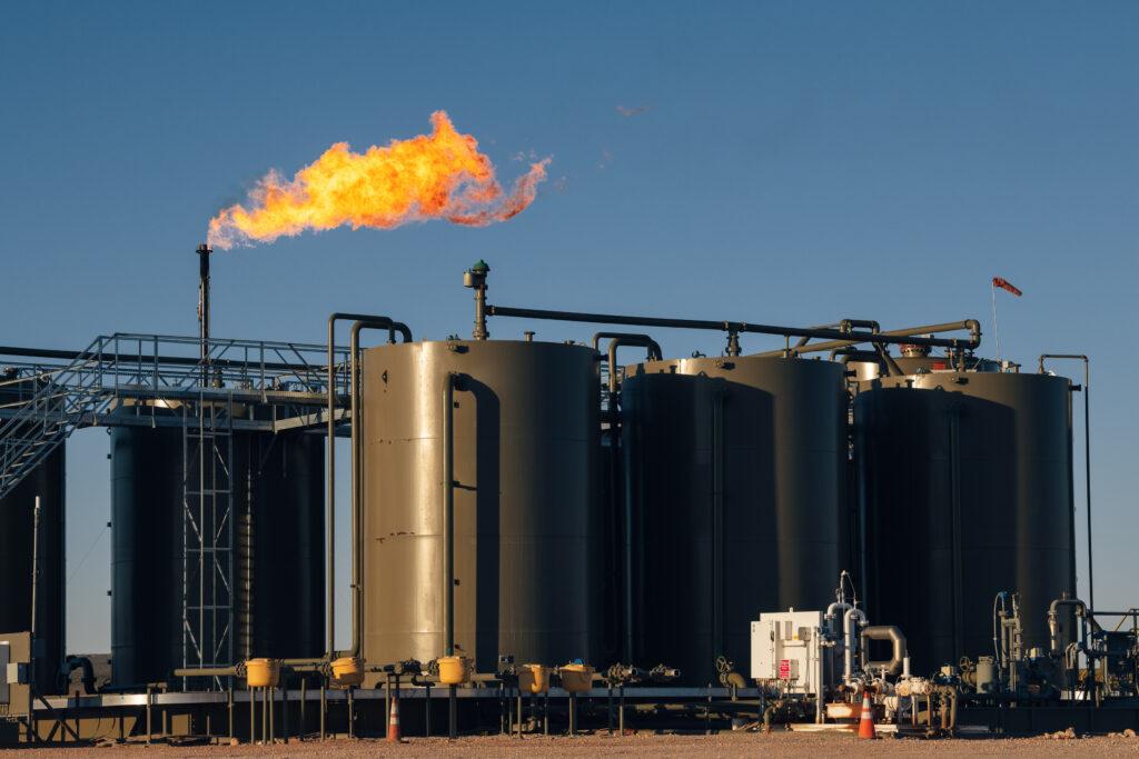 Flare burns over oilfield storage tanks.