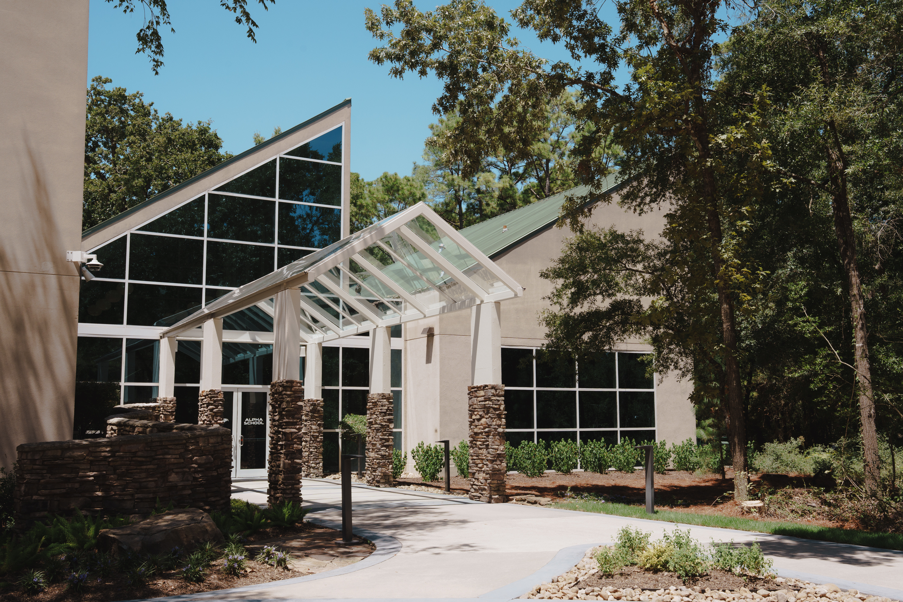 A geometric building with glass windows is surrounded by trees.