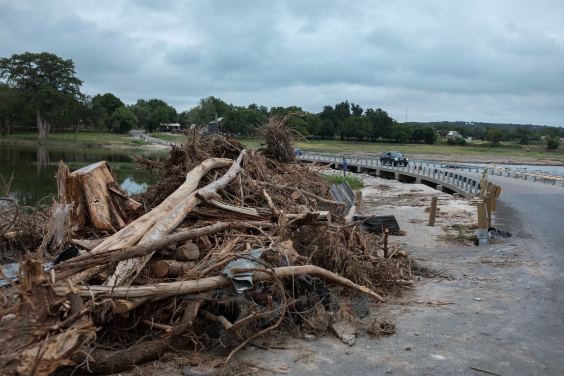 Dead trees, driftwood and other vegetation are piled high beside a curve in the road on a cloudy day.