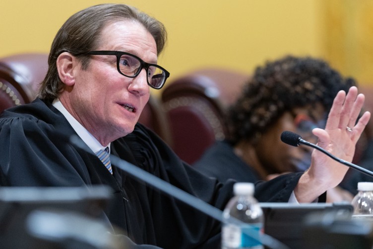 A man in judicial robes raises his hand while speaking in a government building.