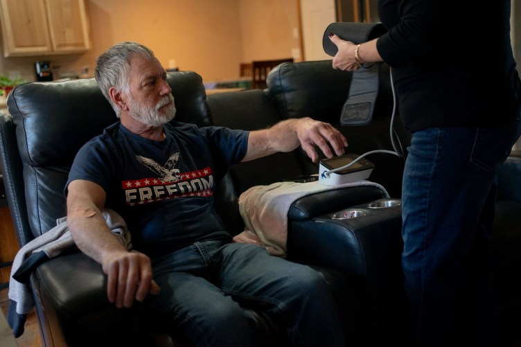 A woman holds a blood pressure cuff while Lonnie Rouse raises his arm to allow her to put the cuff on.