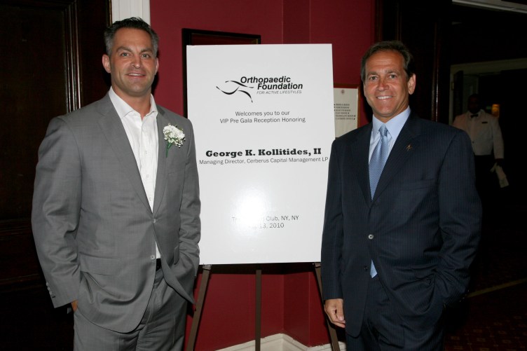 Two men in suits stand, smiling at the camera, in front of a sign that reads “Orthopaedic Foundation” and “George K. Kollitides, II.”
