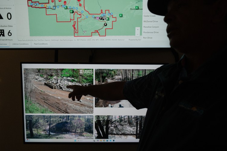 An official points toward digital displays showing maps and real-time U.S. Geological Survey river-monitoring feeds.