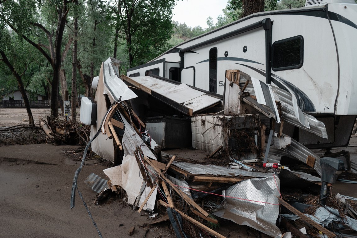 A heavily damaged trailer surrounded by flood debris, mud and torn structural materials.